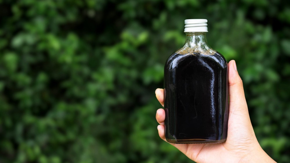 A hand holds cold brew coffee in a glass bottle outside