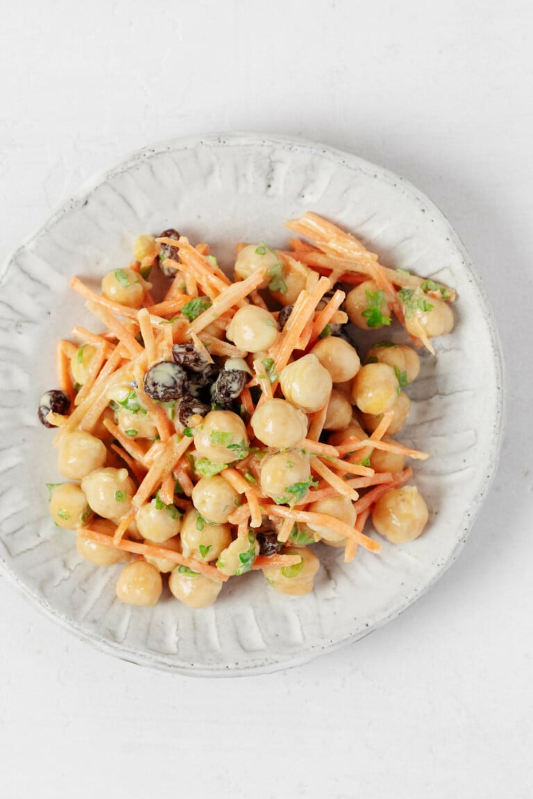 An overhead image of a creamy mixture of chickpeas, raisins, parsley, and grated carrots.