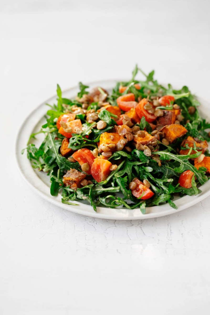 An angled photograph of a white plate covered with a plant-based, lentil tahini sweet potato salad..